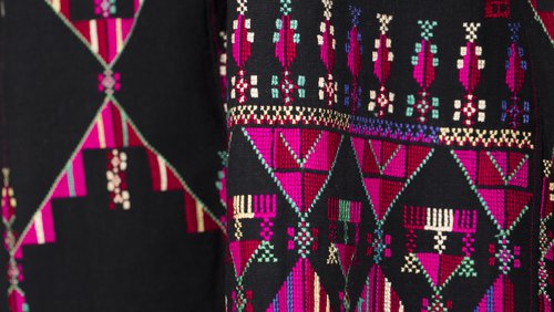 Intricate pink, purple, green and yellow embroidery is shown on rich black material.