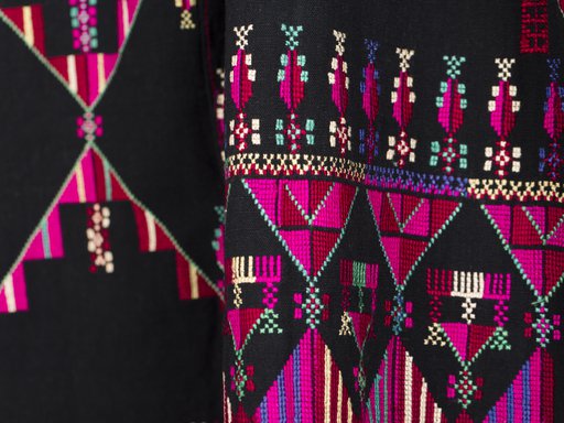 Intricate pink, purple, green and yellow embroidery is shown on rich black material.