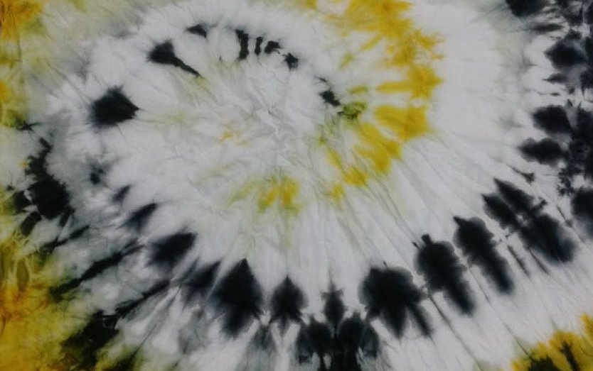 A close-up of a yellow and black tie-dyed shirt with a spiral design