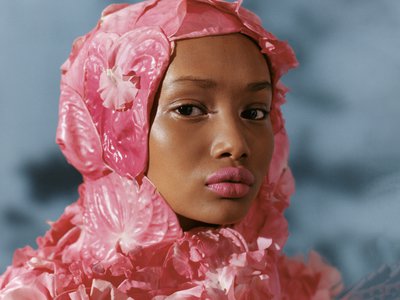 A young black woman with pink lipstick wears a hijab made from large exotic pink flowers.