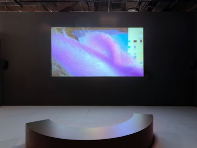 View of an artwork projected on a wall in a dark space with contemporary seating.