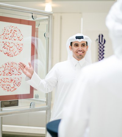 A man in traditional Qatari attire shows visitors some Arabic calligraphy